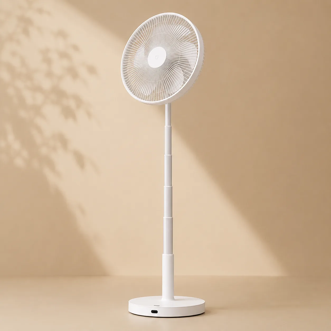 Ventilateur sur pied blanc devant un mur beige traversé par des ombres de feuillage